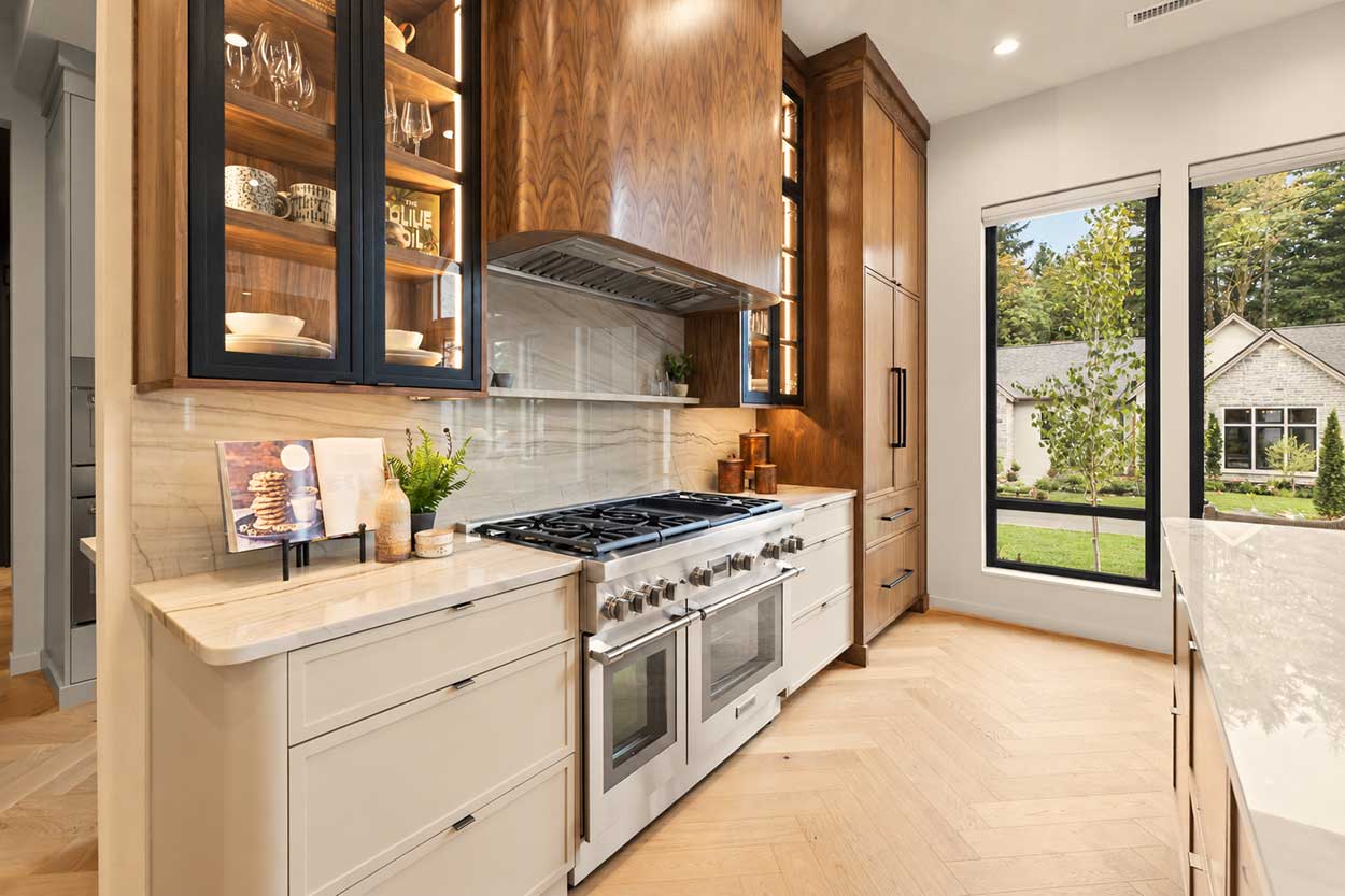 Range wall with a professional gas range, quartzite slab backsplash, curved walnut hood, and lit glass-front cabinets.
